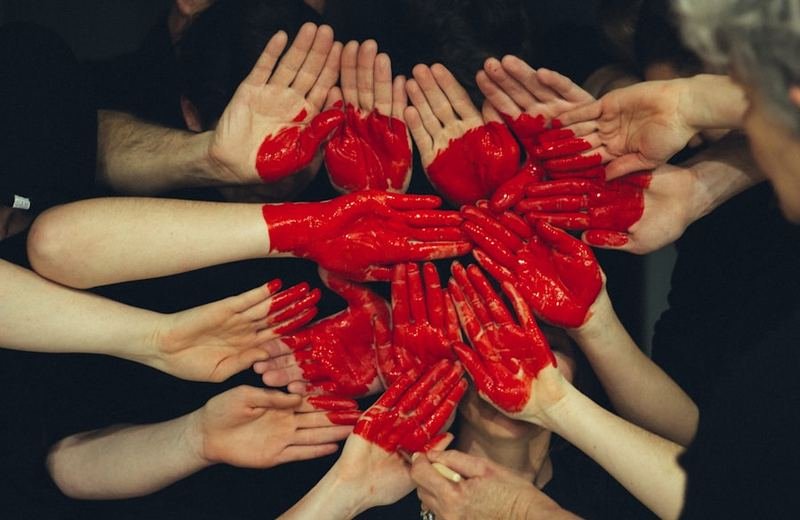 Many hands together painted as one red heart